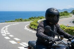 海沿いのワインディングロードを走るバイクライダー。バイクグローブを着用してハンドルを操作。