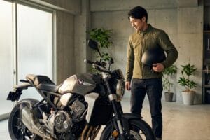ガレージ内のネイキッドバイクとヘルメットを持つ男性。バイク買取の売却前に車両状態を確認している。